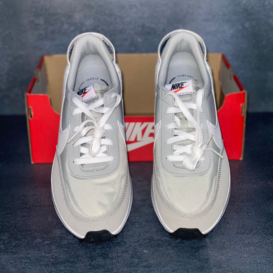 Grey and white Nike sneakers with an orange Nike sneaker box. The sneaker box has no lid.