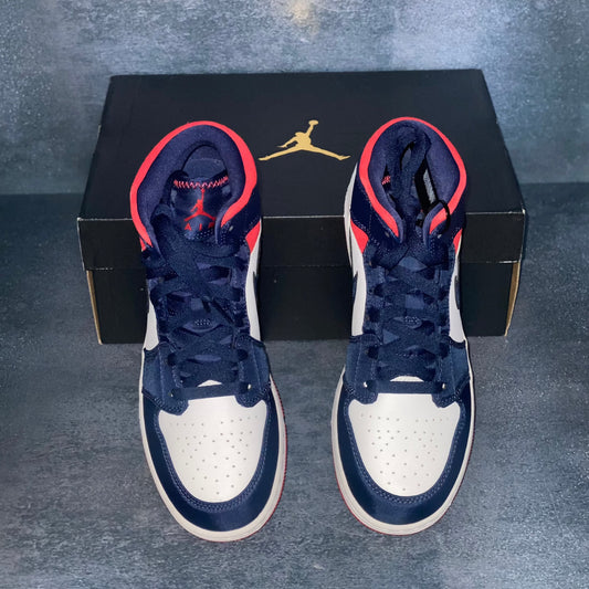 Red, white, and blue Nike Air Jordan 1 Mid sneakers with a black Air Jordan sneaker box.