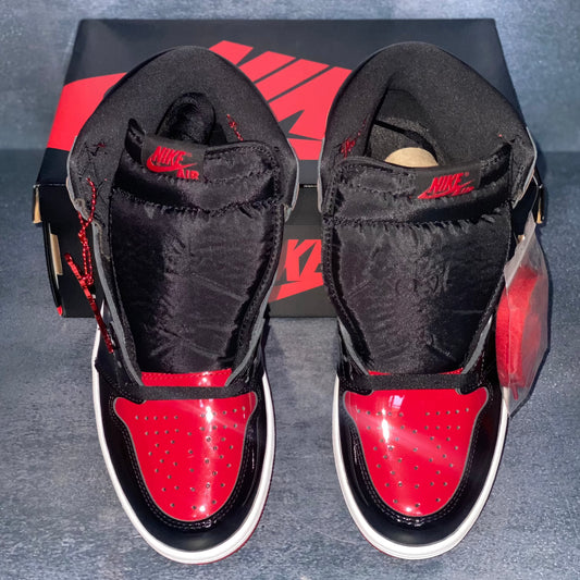 Black and red patent leather Nike Air Jordan 1 Retro High sneakers with a black and red Nike Air Jordan sneaker box.