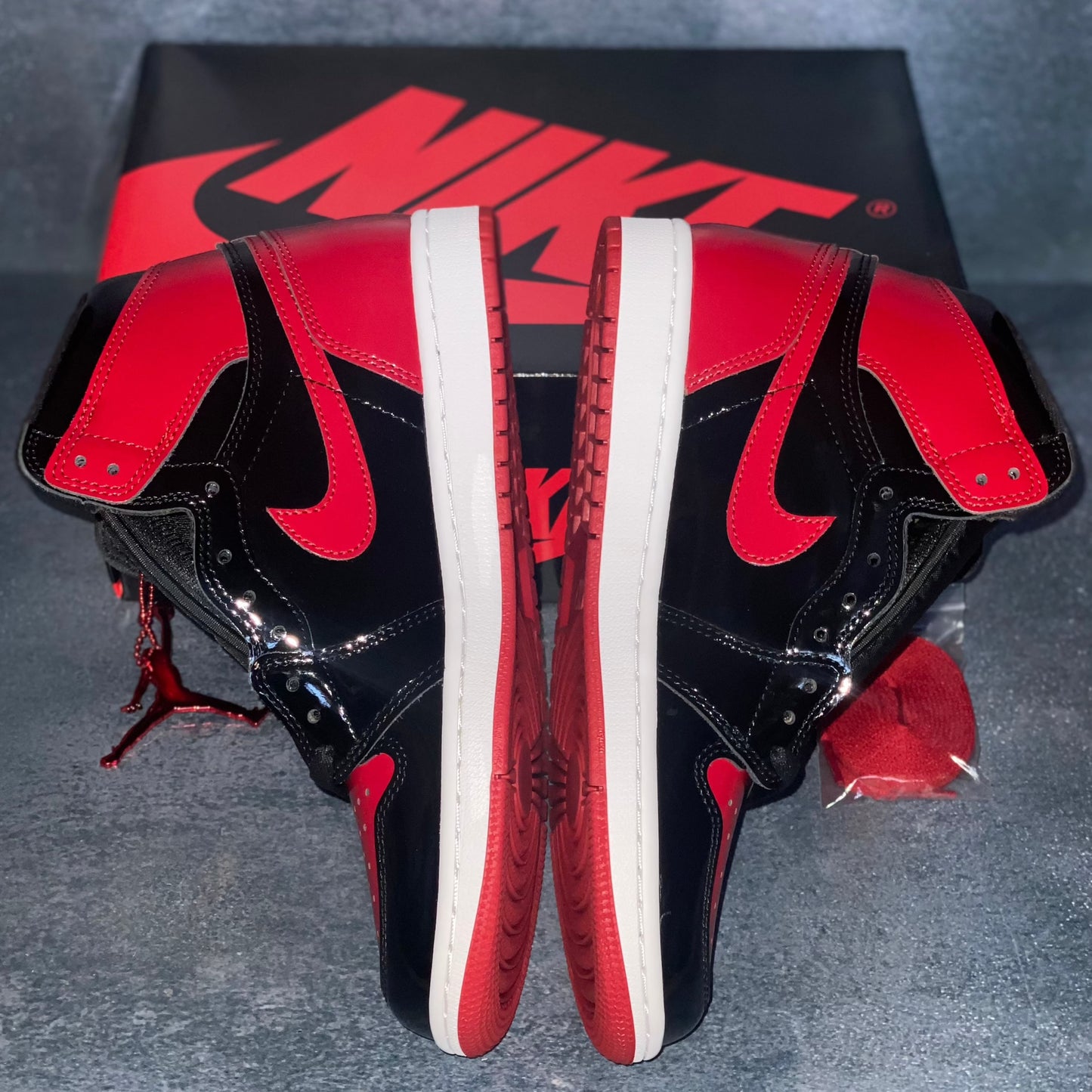 The medial side of the black and red patent leather Nike Air Jordan 1 Retro High sneakers with a black red Nike Air sneaker box.