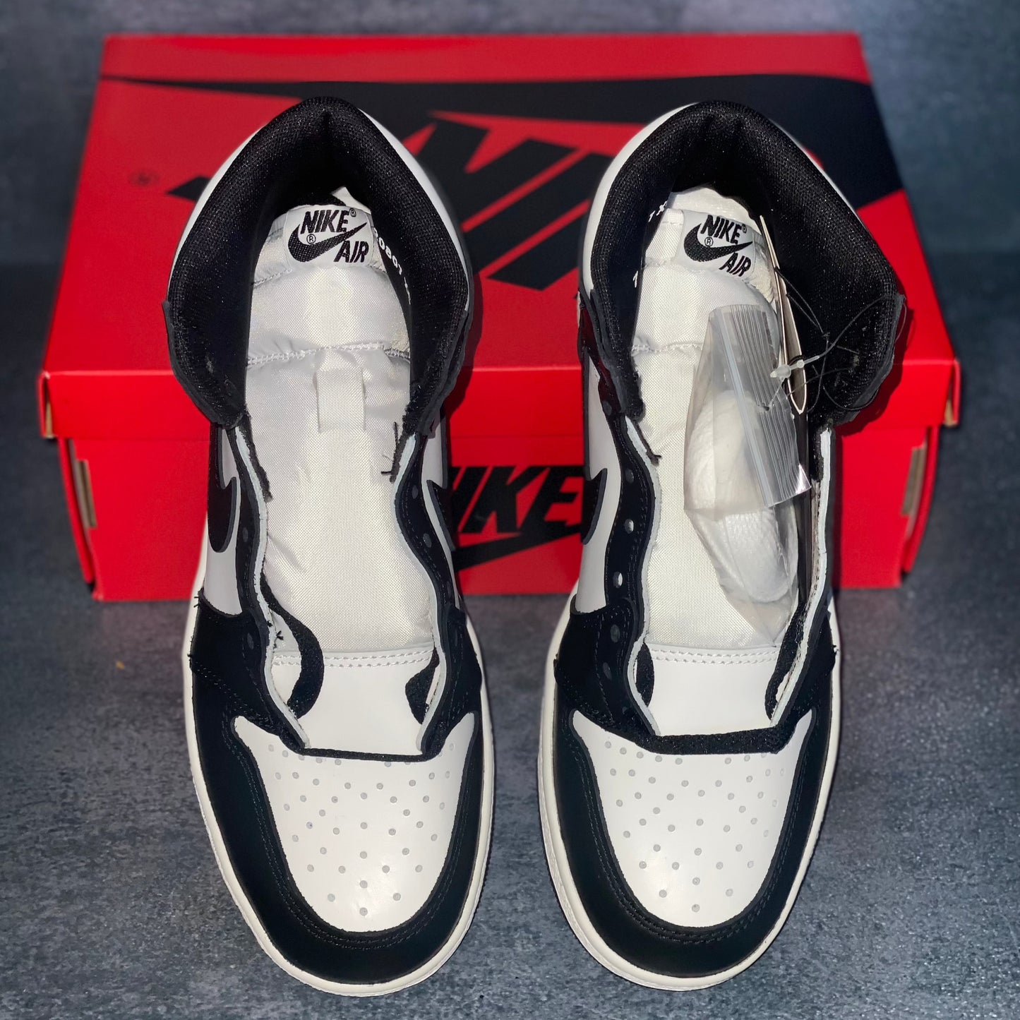 Black and white Nike Air Jordan 1 Retro High 85 sneakers with a red and black Nike Air Jordan sneaker box.