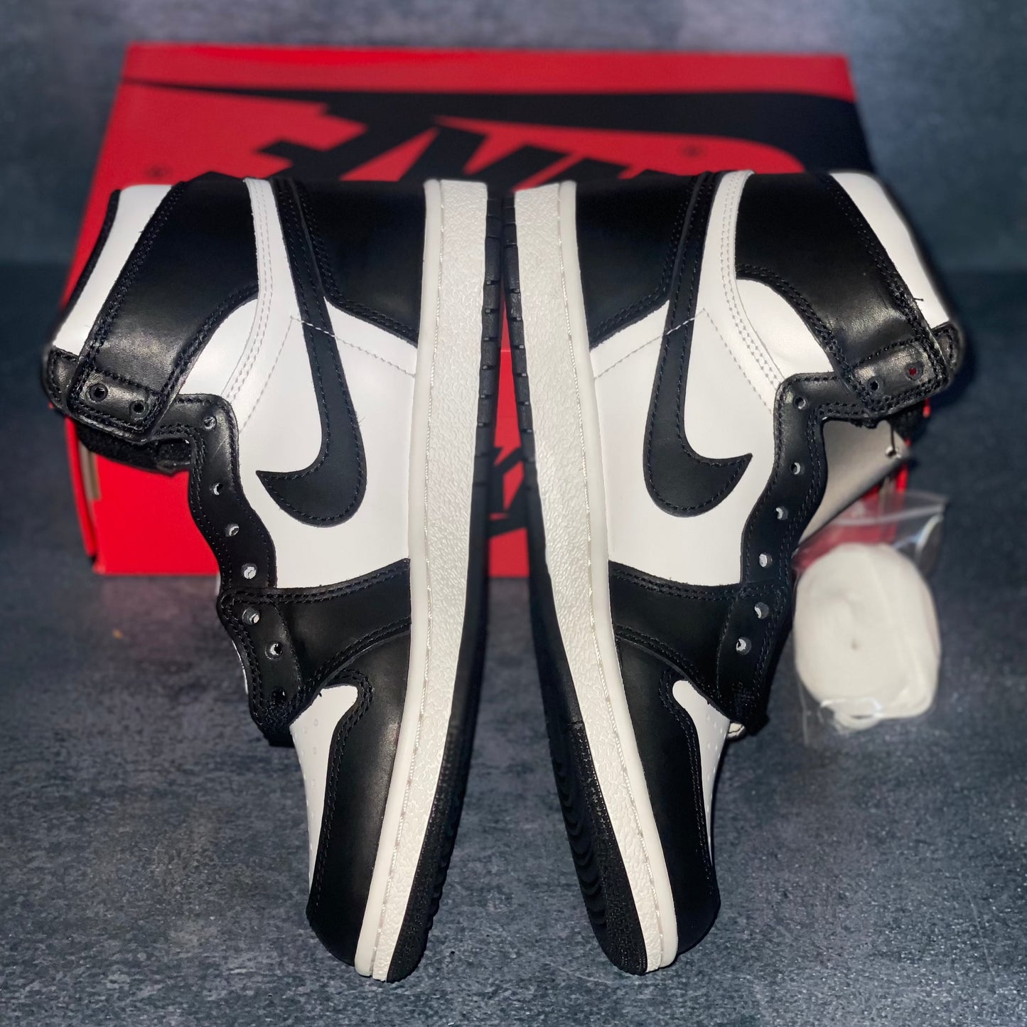 The medial side of the black and white Nike Air Jordan 1 Retro High 85 sneakers with a red and black Nike Air Jordan sneaker box.