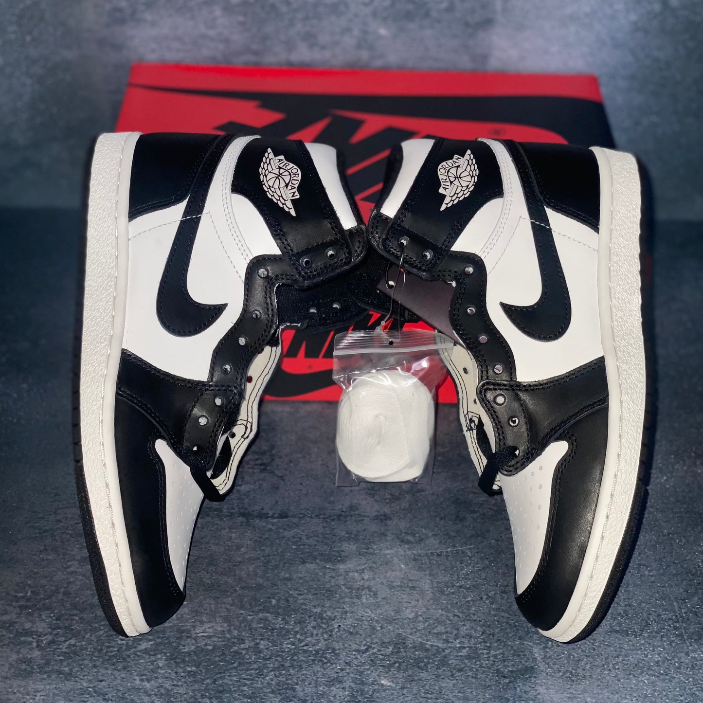 The lateral side of the black and white Nike Air Jordan 1 Retro High 85 sneakers with a red and black Nike Air Jordan sneaker box.