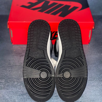 The black sneaker bottom of the black and white Nike Air Jordan 1 Retro High 85 sneakers with a red and black Nike Air Jordan sneaker box.