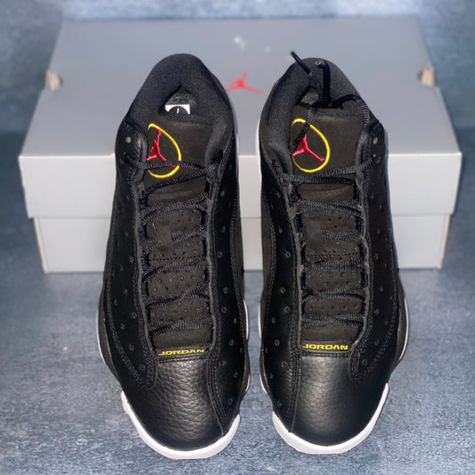 Black Air Jordan 13 sneakers with yellow and red accents and a light grey Air Jordan sneaker box.